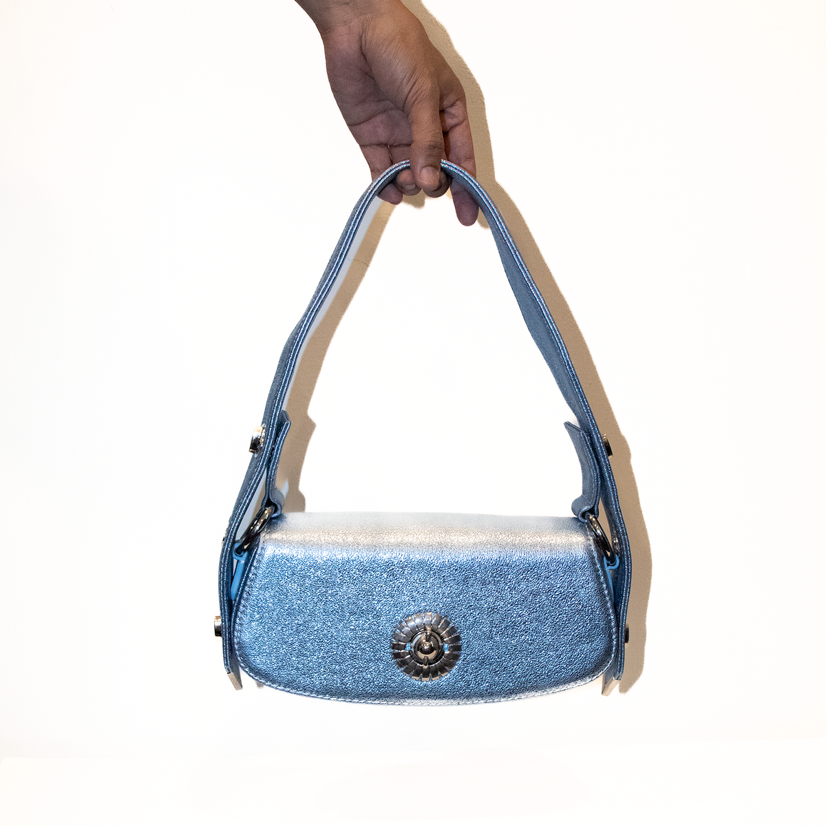 Blue, glittery leather handbag held by a hand on a white background