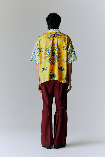 Person wearing a bright yellow floral shirt and burgundy pants on a plain background